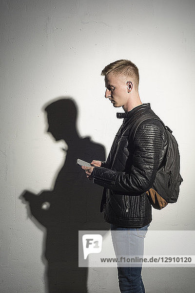 Young man with backpack wearing black leather jacket looking at cell phone