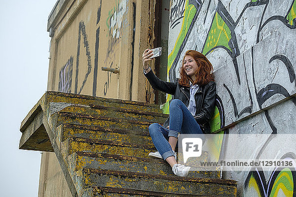 Italy  Finale Ligure  redheaded teenage girl ltaking selfie in front of graffiti wall