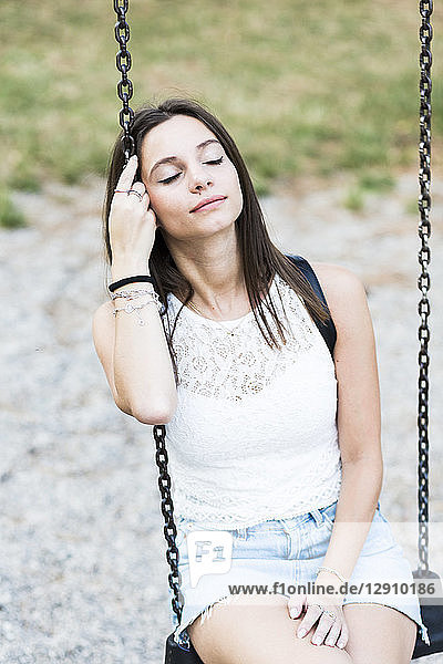 Young woman with closed eyes sitting on a swing on a playground