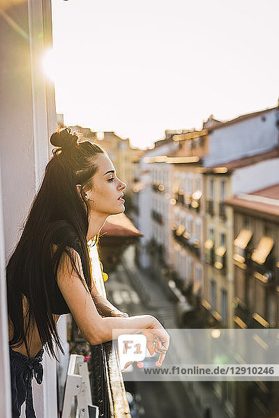 Beautiful young woman on balcony above the city at sunset