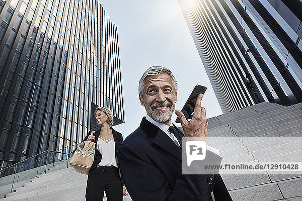 Portrait of content businessman on the phone with his business partner in the background