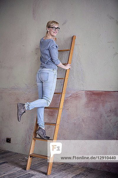 Smiling woman standing on ladder in an unrenovated room of a loft