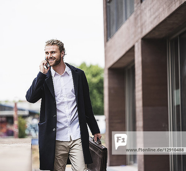 Smiling young businessman on cell phone outside office building