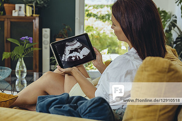 Woman looking at ultrasound picture of unborn child on couch