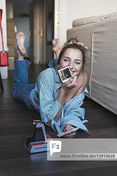 Portrait of happy young woman lying on the floor with instant photos of herself
