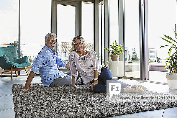 Portrait of smiling mature couple relaxing at home sitting on carpet