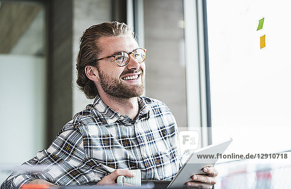 Smiling businessman holding tablet in office