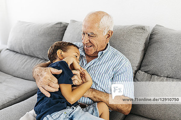 Grandson and grandfather laughing while tickling each other on the couch