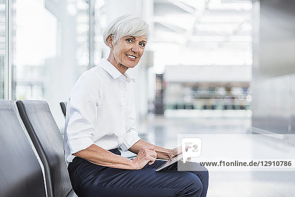 Smiling senior businesswoman sitting in waiting area using tablet