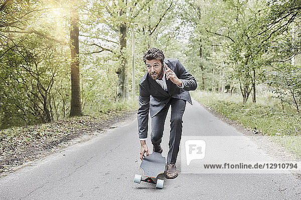 Businessman walking with skateboard and smartphone on rural road