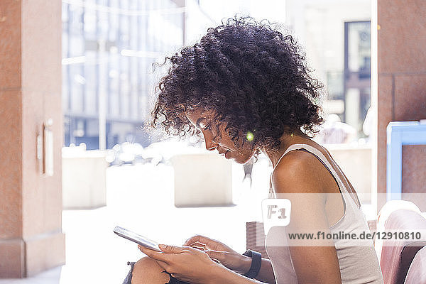 Young woman with curly hair sitting at sidewalk cafe using digital tablet
