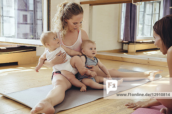Mother with twin babies sitting on yoga mat