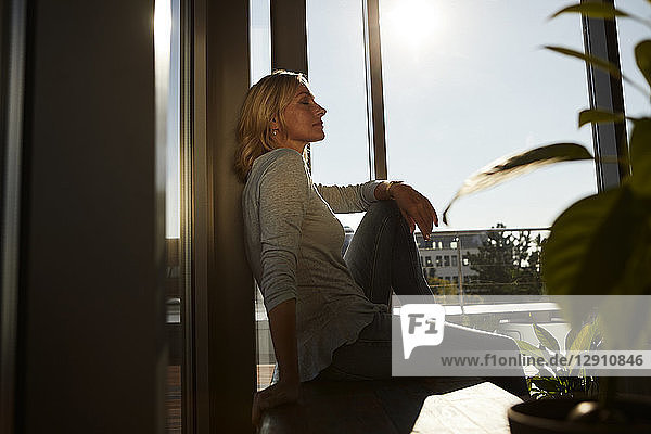 Relaxed mature woman sitting in sunlight at home