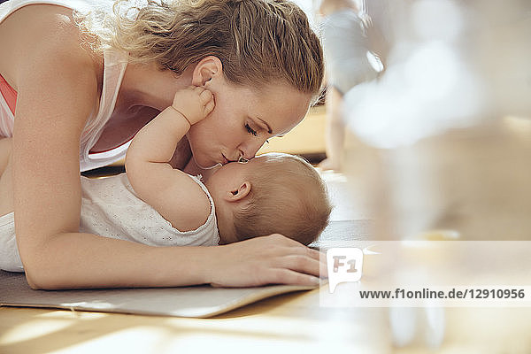 Mother kissing her baby while working out on a yoga mat