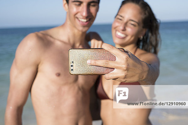 Happy young couple taking selfies on the beach
