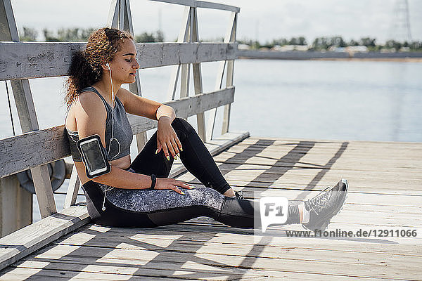 Young athletic woman wearing earbuds resting at the riverside