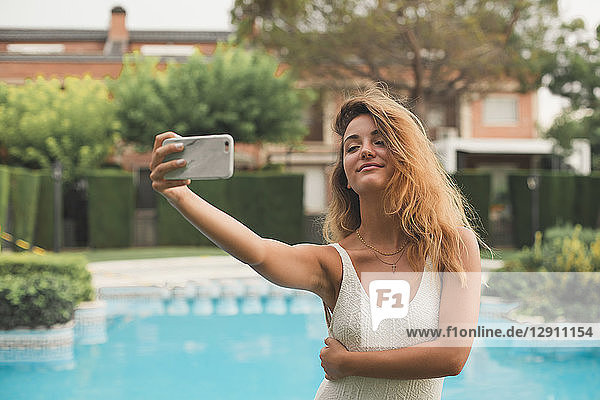 Portrait of young woman in a swimsuit making a selfie with the pool in the background