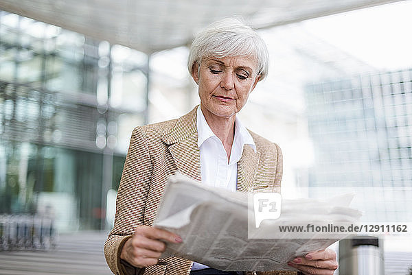 Senior businesswoman in the city reading newspaper