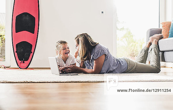 Mother and daughter using laptop  lying on carpet