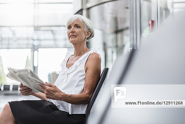 Senior woman sitting in waiting area with newspaper