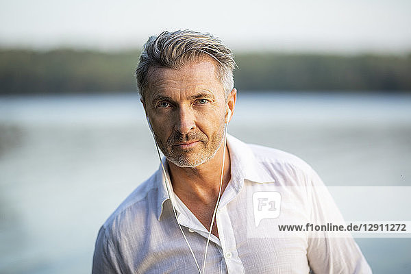 Portrait of man listening music with earphones at lake