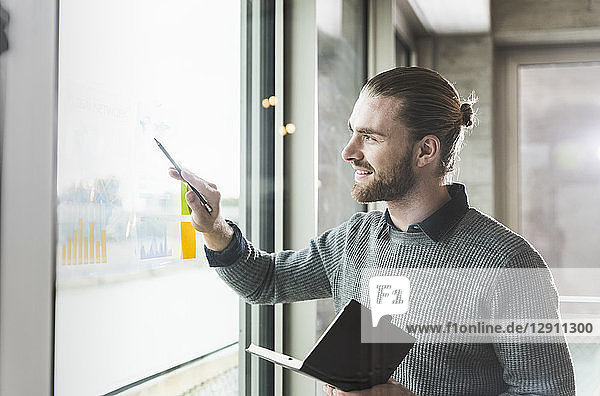 Smiling young businessman working on data at windowpane