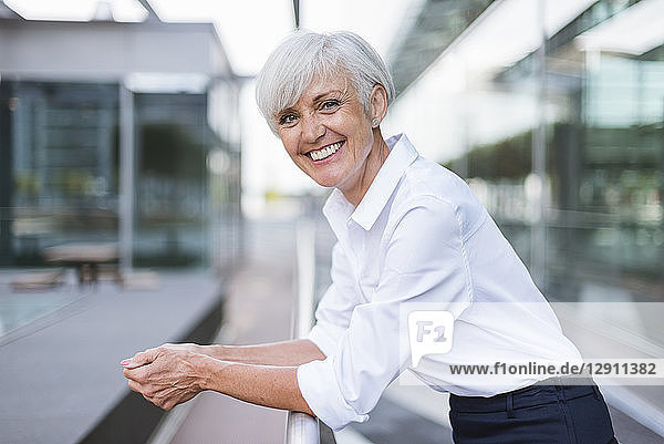 Portrait of happy senior woman leaning on railing in the city