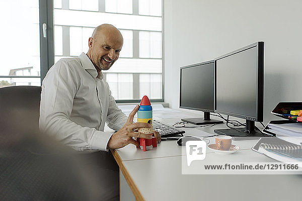 Businessman sitting at desk  looking at toy rocket