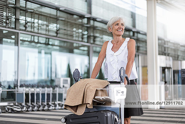 Smiling senior woman pushing baggage cart at the airport
