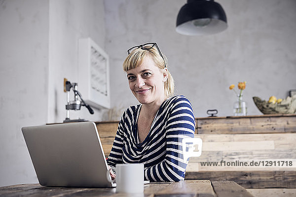 Portrait of smiling woman sitting at table with laptop and coffee mug