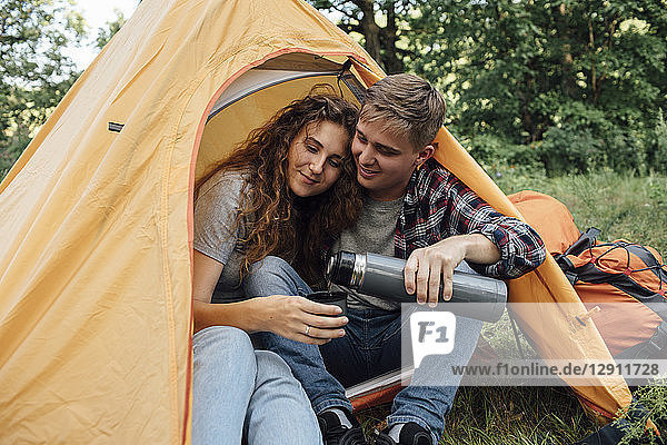 Young couple sitting in tent  drinking tea