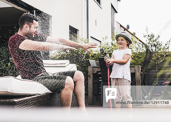 Fathercand daughter in the garden  daughter splashing water with hose