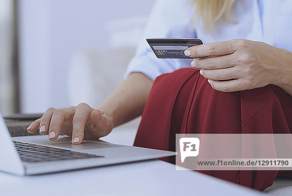 Blond woman sitting on couch  using laptop to make a payment with her credit card