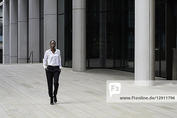 Businesswoman wearing white shirt and black trousers walking in front of a modern office building