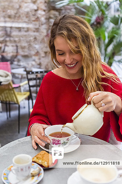 Smiling young woman pouring tea into a cup at pavement cafe
