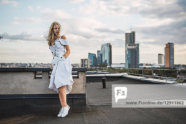 Blond young woman standing on roof terrace wearing white dress