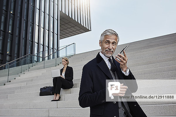 Portrait of businessman on the phone while business woman working on laptop in the background