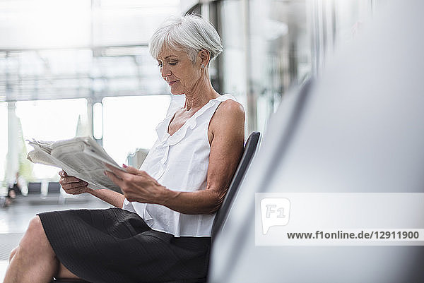 Senior woman sitting in waiting area reading newspaper