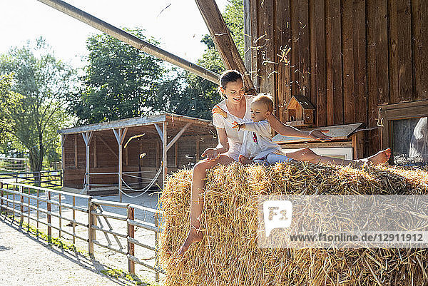 Happy mother and little daughter playing with straw in a barn