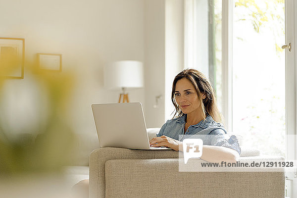Mature woman sitting on couch at home using laptop