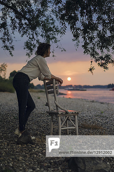 Woman leaning on a chair at the river  watching sunset