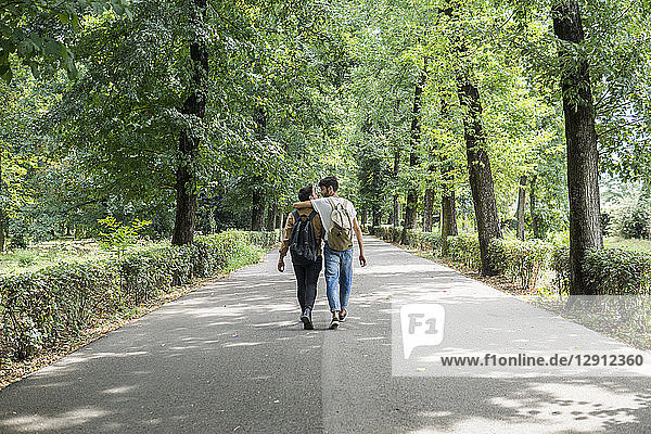 Back view of young gay couple with backpacks walking on a road