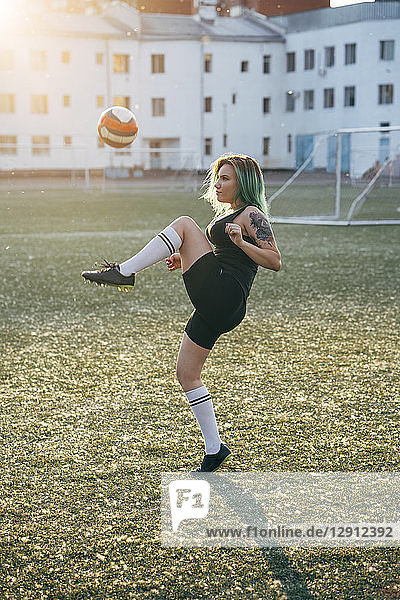 Young woman playing football on football ground balancing the ball