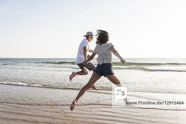 Young couple having fun on the beach  running and jumping at the sea