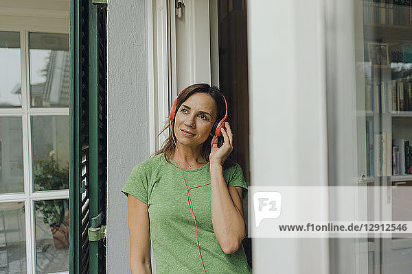 Mature woman standing at terrace door listening to music with headphones