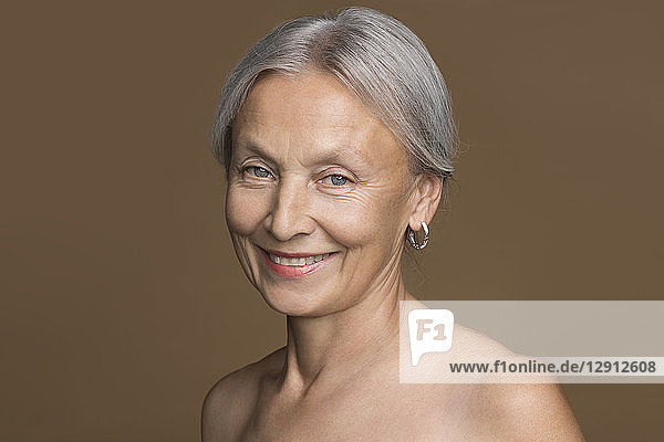Portrait of naked senior woman with grey hair in front of brown background