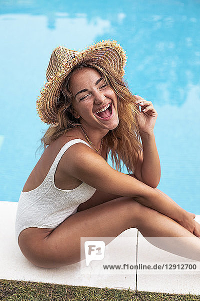Young girl smiling with straw hat and swimsuit sitting at poolside