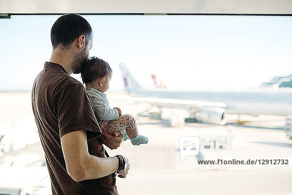 Man holding a baby girl at the airport  looking at the airplanes