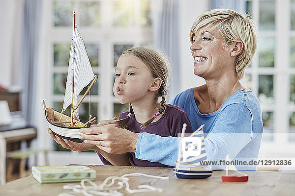 Happy mother and daughter playing with model boat at home