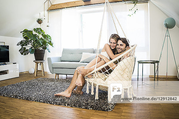Happy affectionate couple sitting in hanging chair at home